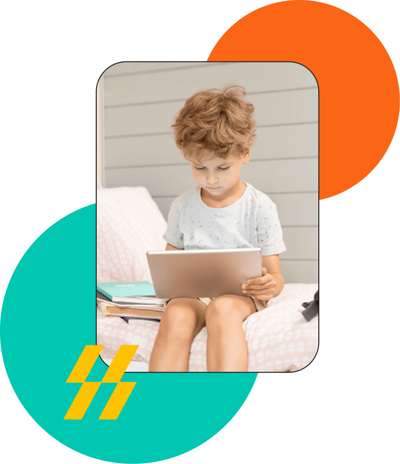 A young child sitting on a bed, looking down at a tablet resting on their lap