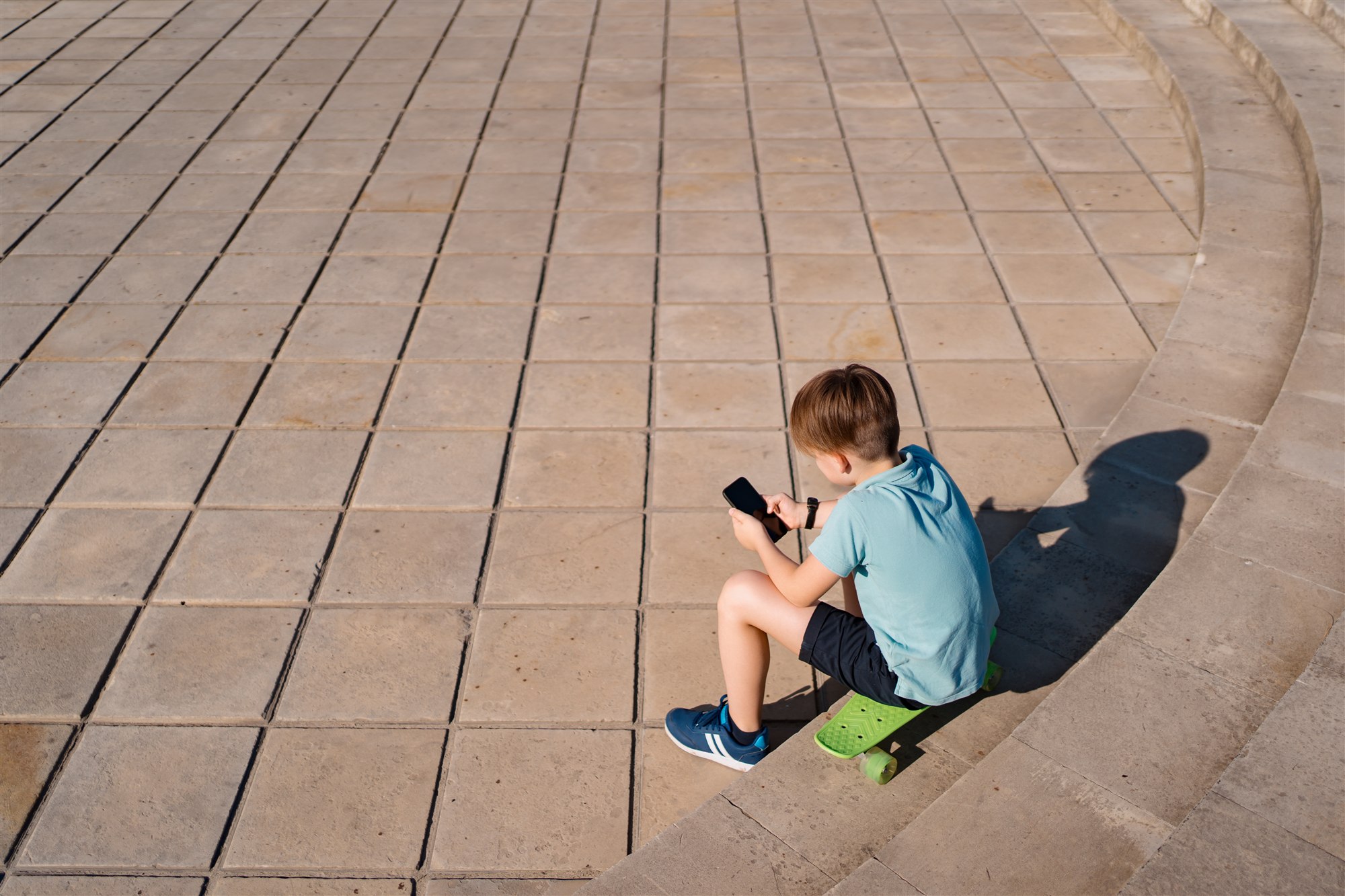 A child sitting on a skateboard looking at a phone